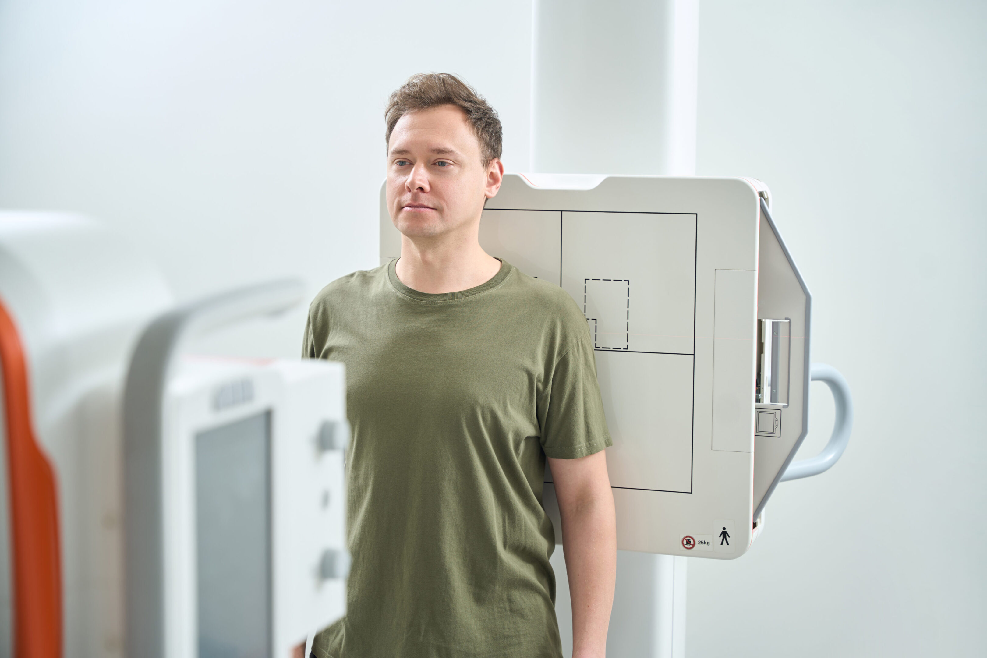Male getting shoulder x-ray in anteroposterior projection Waist-up portrait of patient leaning his back against image receptor in front of radiography machine